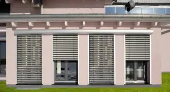 Fassade eines Hauses mit vier Fenstern, die jeweils mit silbernen Außenjalousien versehen sind.