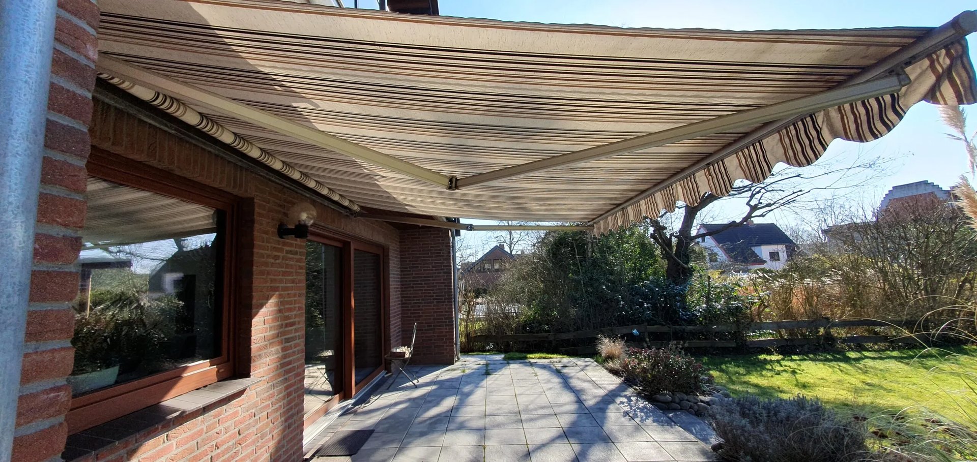 Ausgefahrene braun-beige gestreifte Markise über einer Terrasse eines Backsteinhauses
